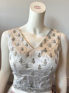 A silver color blouse Product details Fabric - silk blend Embroidery - Thread and stones  Bust size 36" Waist 32" Can be tailored to fit 38" For extra charges Elegant Embroidered V-neck Blouse Piece, Elegant Fitted Silver Top, Elegant Silk Blouse With Pearl Embroidery, Silver Blouse Piece With Mirror Work For Reception, Elegant Sleeveless Blouse With Pearl Embroidery, Silk Blouse Piece With Pearl Embroidery, Silver Silk Blouse Piece For Wedding, V-neck Tops With Mirror Work For Wedding, Elegant Silver Blouse For Reception