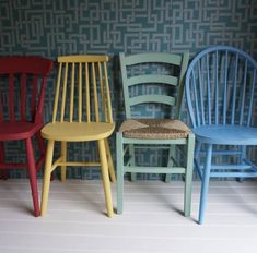 three different colored chairs sitting next to each other in front of a wallpapered room