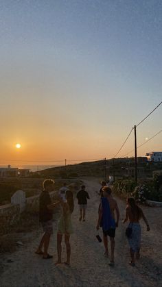 a group of people walking down a dirt road near the ocean at sunset or dawn