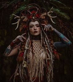 a woman with long hair and tattoos standing in the woods holding her hands on her head