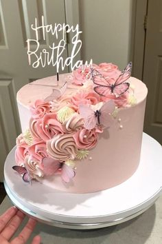 a birthday cake with pink flowers and butterflies on top is being held up by someone's hand