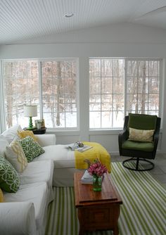 a living room filled with furniture and windows covered in white coverings next to a green striped rug