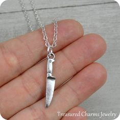 a hand holding a silver necklace with a knife on it