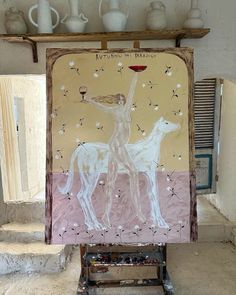 a painting is displayed on an easel in front of a wall with vases