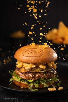 a burger topped with cheese and lettuce on a black plate next to chips