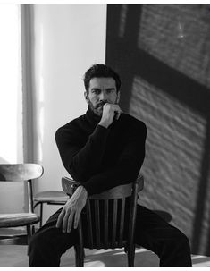 a black and white photo of a man sitting in a chair with his hand on his chin