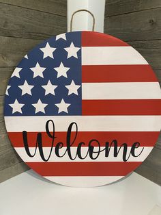 a welcome sign with an american flag painted on the front and back, hanging from a hook