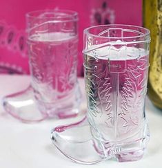 two clear glasses sitting on top of a table next to a pink vase and bottle