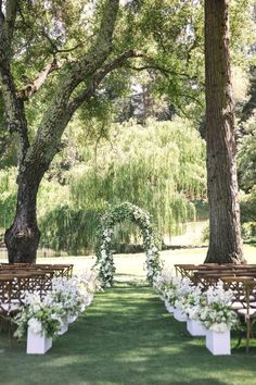 an outdoor ceremony set up with white flowers and greenery on the grass, surrounded by trees