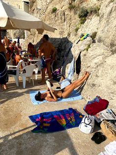 a woman laying on top of a blue towel next to a rocky cliff under an umbrella