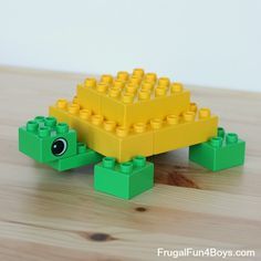 a lego turtle made out of yellow and green bricks on a wooden table with white wall in the background