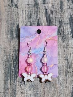 the pink and white earrings are sitting on a piece of wood