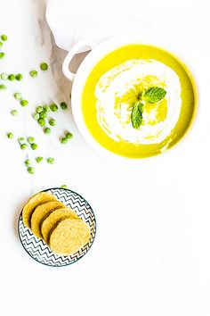 a bowl of soup and some crackers on a plate next to it, with peas scattered around