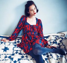 a woman sitting on top of a bed in a red and blue plaid shirt dress