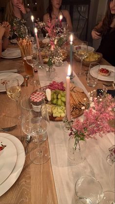 people sitting at a table with food and wine in front of them, all lit up by candles