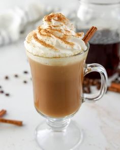 there is a cup of hot chocolate with whipped cream and cinnamon sticks on the side