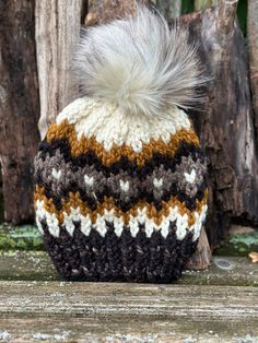 a crocheted hat with a fuzzy pom - pom sits on a wooden surface