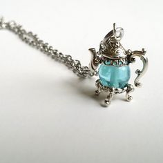 a silver teapot with a blue glass in it's body on a chain