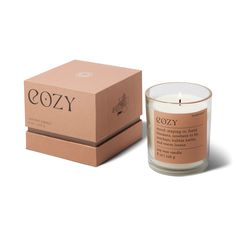 a candle in front of a cardboard box with the word cozy on it and an orange label next to it