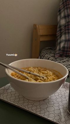 a bowl of noodles with two tongs in it on a tray next to a bottle