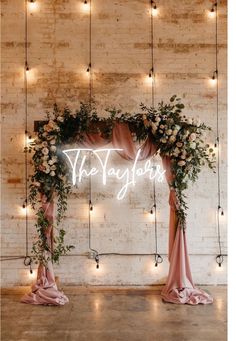 the wedding arch is decorated with flowers and greenery, along with fairy lights hanging from the brick wall