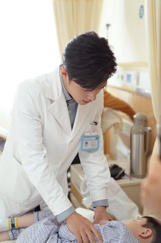 a man in a white lab coat is holding a baby on a hospital bed while another person looks at him