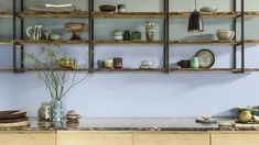 a kitchen with blue walls and wooden shelves filled with plates, bowls, cups and utensils