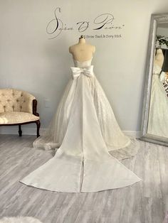 a white wedding dress on display in front of a wall with a mirror and mannequin