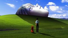 a man standing in front of a giant head on top of a grass covered hill