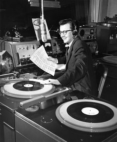 a man sitting at a record player with headphones on and reading a paper in front of him