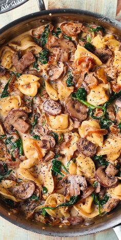 a skillet filled with pasta, mushrooms and spinach