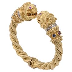 An extremely well made bangle bracelet by iconic Greek jewelry designer Ilias Lalaounis, this bangle depicts 2 Chimera heads atop a textured and twisted 18 karat yellow gold hinged bangle. The chimeras are adorned with vivid red ruby eyes, and diamond, sapphire & ruby collars. The diamonds weigh approximately .14 carats in total and are F-G color and SI clarity. The rubies weigh approximately .28 carats in total. The sapphires weigh approximately .16 carats in total. The bracelet is marked Lalao Luxury Intaglio Bangle Jewelry, Designer Bangle Bracelet With 17 Jewels, Greek Jewelry Designers, Tech Pack, Greek Jewelry, Ruby Sapphire, Gold Bangle Bracelet, Ruby Diamond, Red Ruby