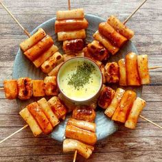 several skewered food items on a blue plate with a small bowl of dipping sauce