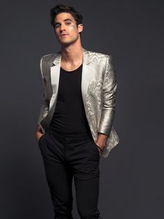 a man in a silver blazer and black pants posing for a photo with his hands in his pockets