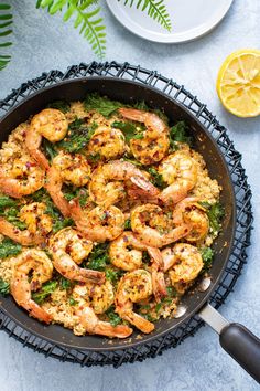 a skillet filled with shrimp and rice on top of a table next to lemon wedges