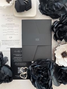 the wedding stationery is surrounded by black flowers and silver brooches, which are accented with an embellished diamond ring