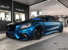 a blue mercedes benz coupe parked in front of a hublot store with its lights on