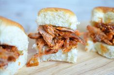 three pulled pork sandwiches sitting on top of a wooden cutting board