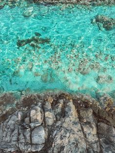 an aerial view of the ocean with rocks and clear blue water in the foreground