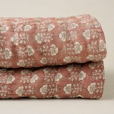 two pink bedspreads with white flowers on them, one is folded and the other has