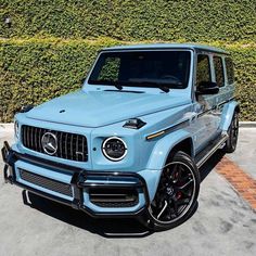 a light blue mercedes g - class is parked in front of a hedge