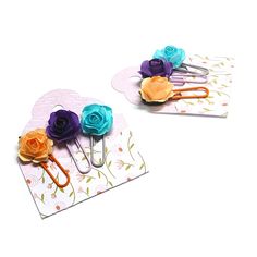 two paper clips with flowers on them sitting next to each other