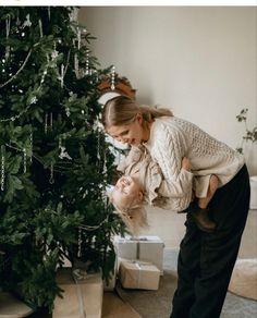 a woman holding a baby next to a christmas tree