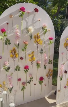 flowers are arranged on the side of a white arch with glass vases and candles