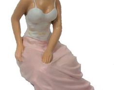 a figurine of a woman in a white top and pink skirt sitting down