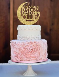 a three tiered cake with pink frosting and gold glitter on top is sitting on a table