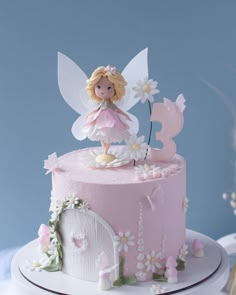 a pink cake with a fairy figurine on top and daisies around it