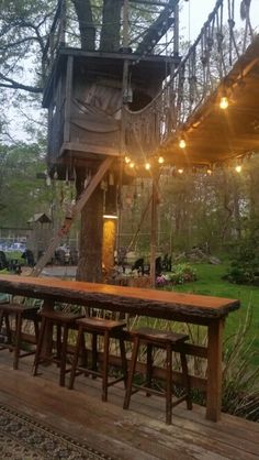 a tree house with lights strung from the roof and wooden benches on the ground below it