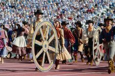 a group of men and women dressed in costume walking on a track with large wheels