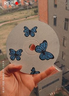 a hand holding a disc with blue butterflies on it in front of a cityscape